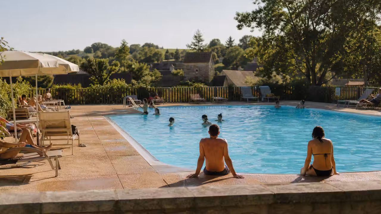 Bassin extérieur bordé de végétation avec des baigneurs vus de dos dans un camping estival