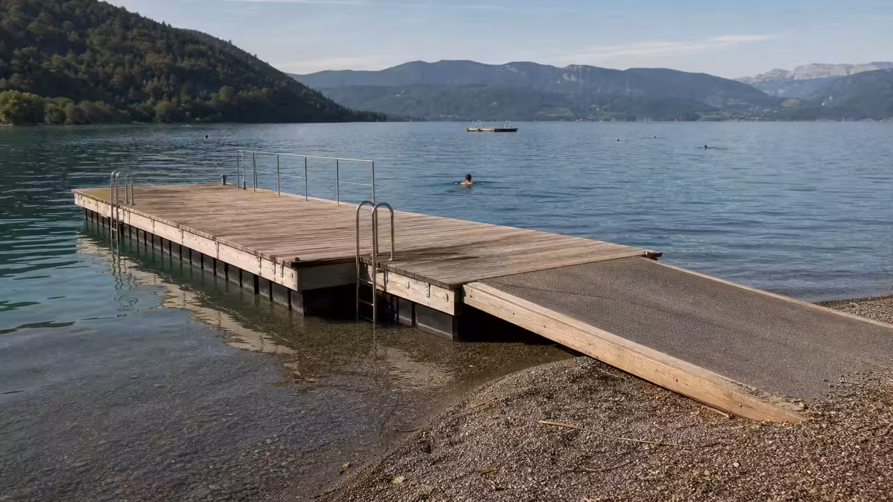 Bassin de baignade flottant relié à une berge sur un lac calme, avec pontons et garde-corps discrets