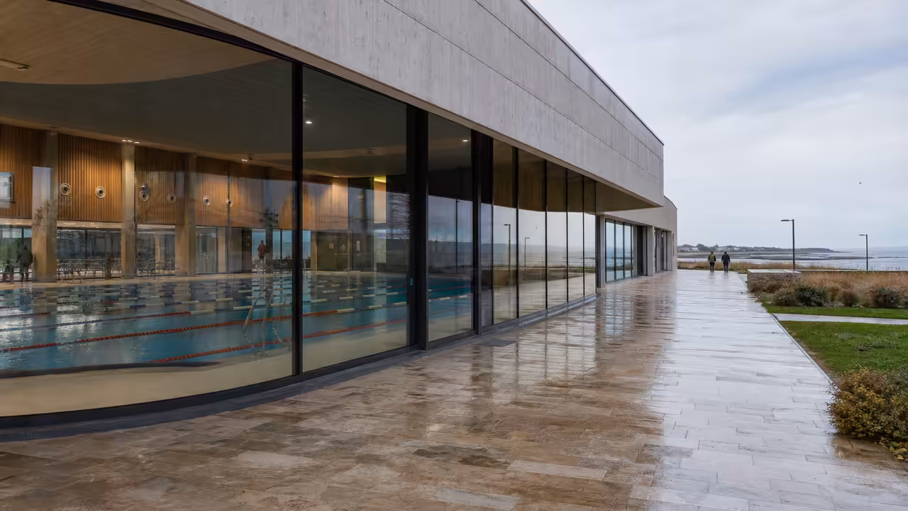Bassin couvert de piscine municipale avec lignes d’eau, baies vitrées et équipements techniques visibles