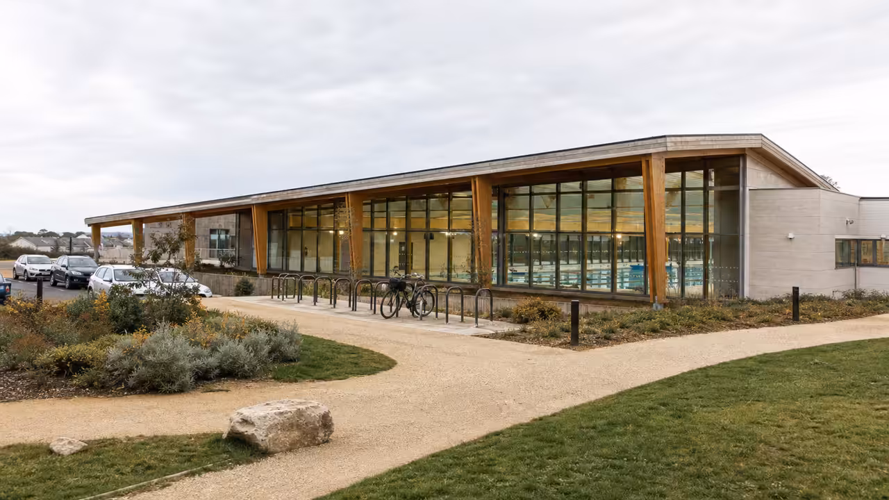 Vue extérieure d’un centre aquatique municipal moderne avec bassins visibles derrière de grandes baies vitrées