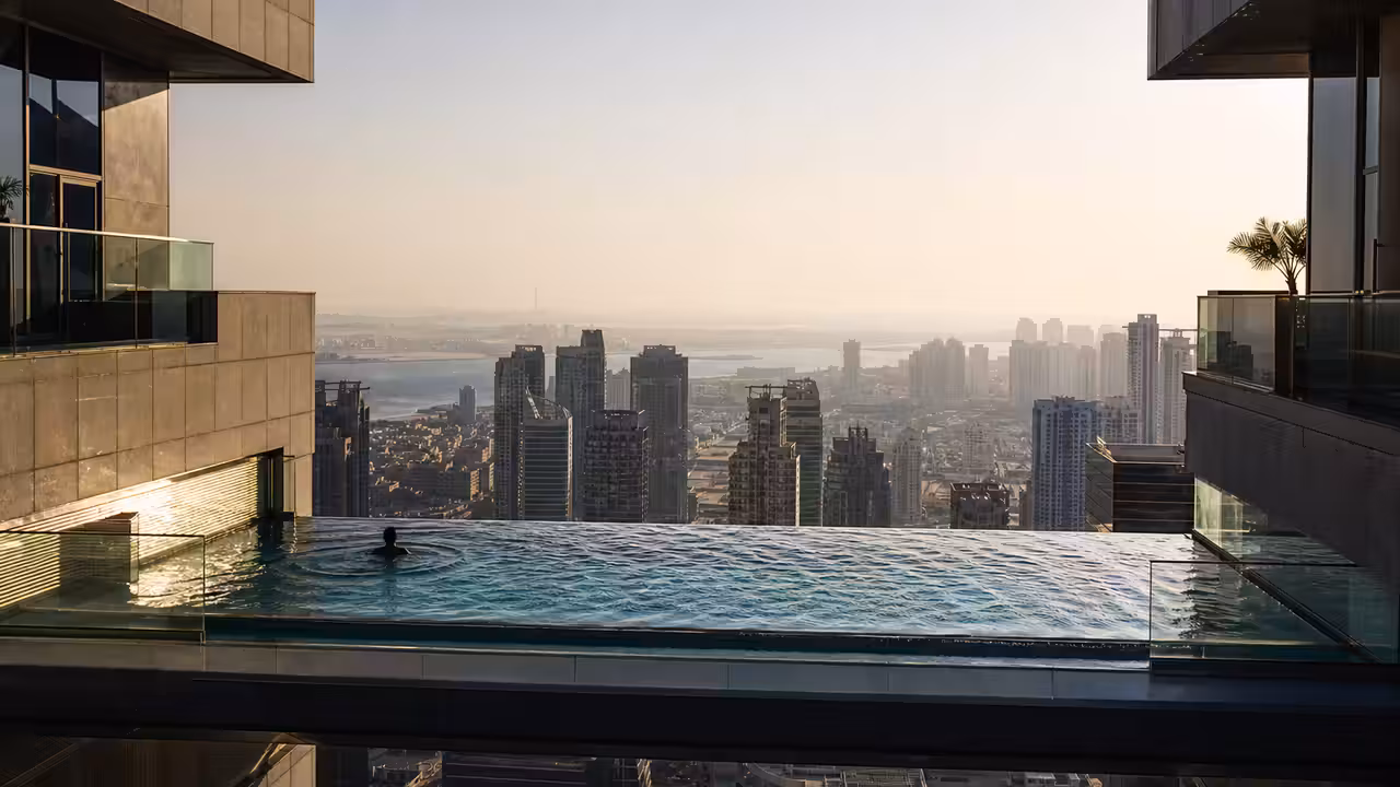 Piscine à débordement suspendue entre deux tours modernes, avec skyline urbaine au soleil couchant