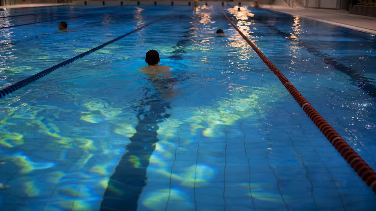 Nageurs dans un bassin couvert éclairé par des projections colorées visibles au fond de l’eau