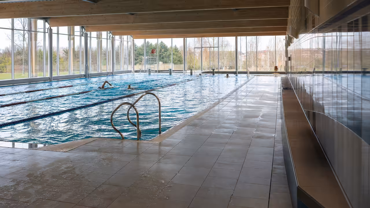 Nageurs en lignes d’eau dans une piscine municipale rénovée, sous une lumière naturelle diffuse