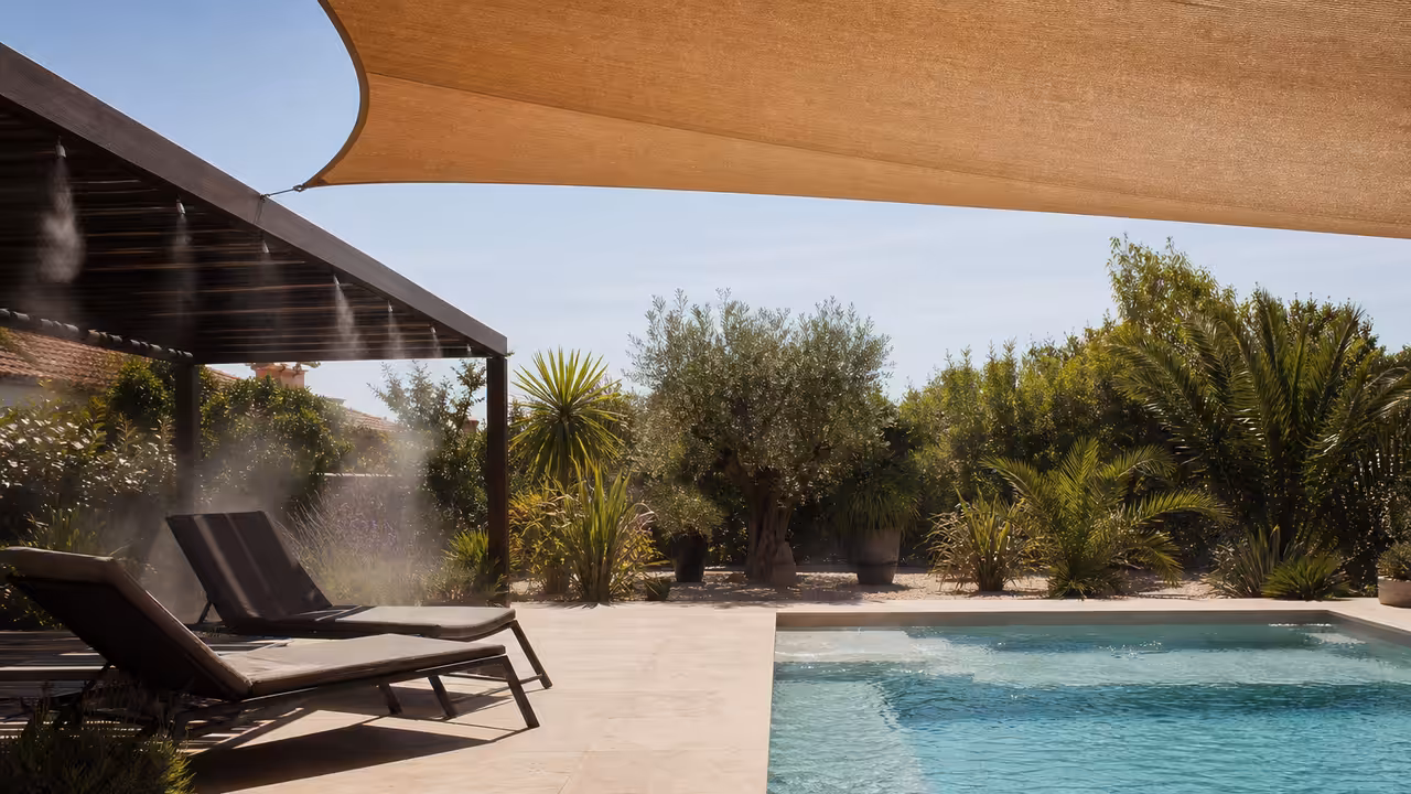 Terrasse ombragée près d’une piscine avec végétation, pergola et fine brumisation lors d’une journée chaude