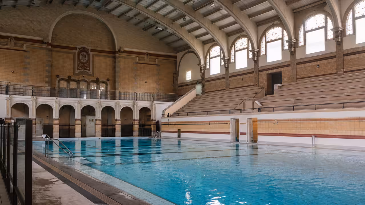 Bassin de piscine publique historique à Toulouse, baigné de lumière naturelle et bordé de gradins vides
