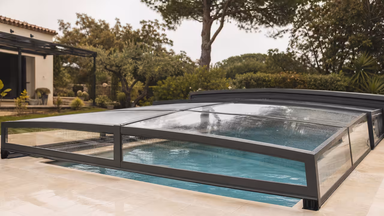 Abri bas télescopique en aluminium fermé sur une piscine familiale entourée d’une terrasse minérale
