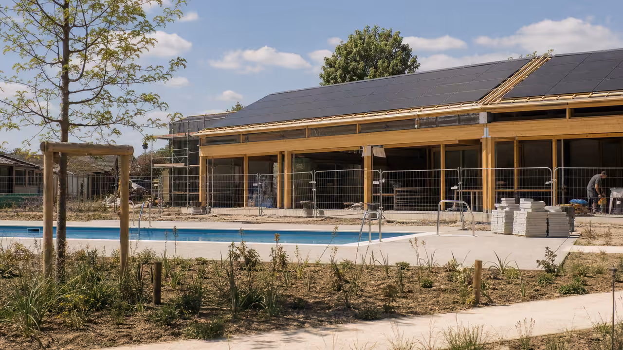 Chantier d’une piscine publique avec structure en bois et toiture photovoltaïque sous une lumière estivale