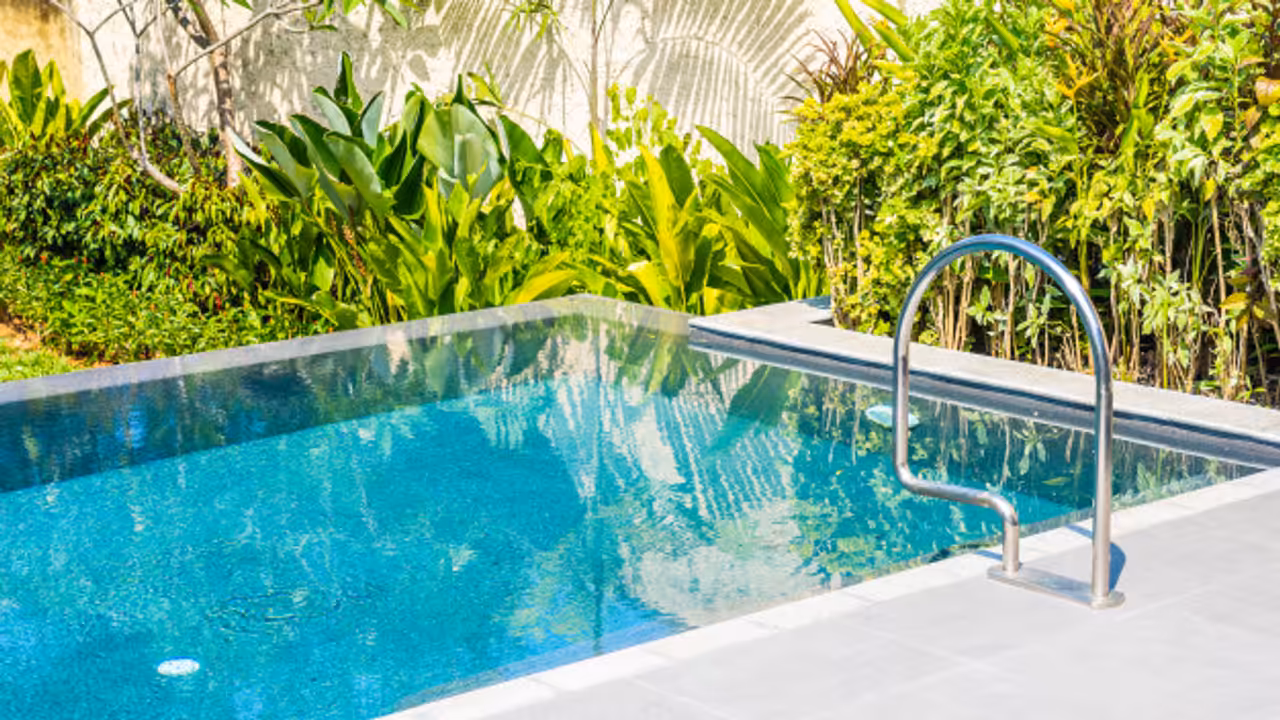 Projecteur LED immergé éclairant en blanc le fond d’une piscine au crépuscule, près d’une terrasse en pierre.