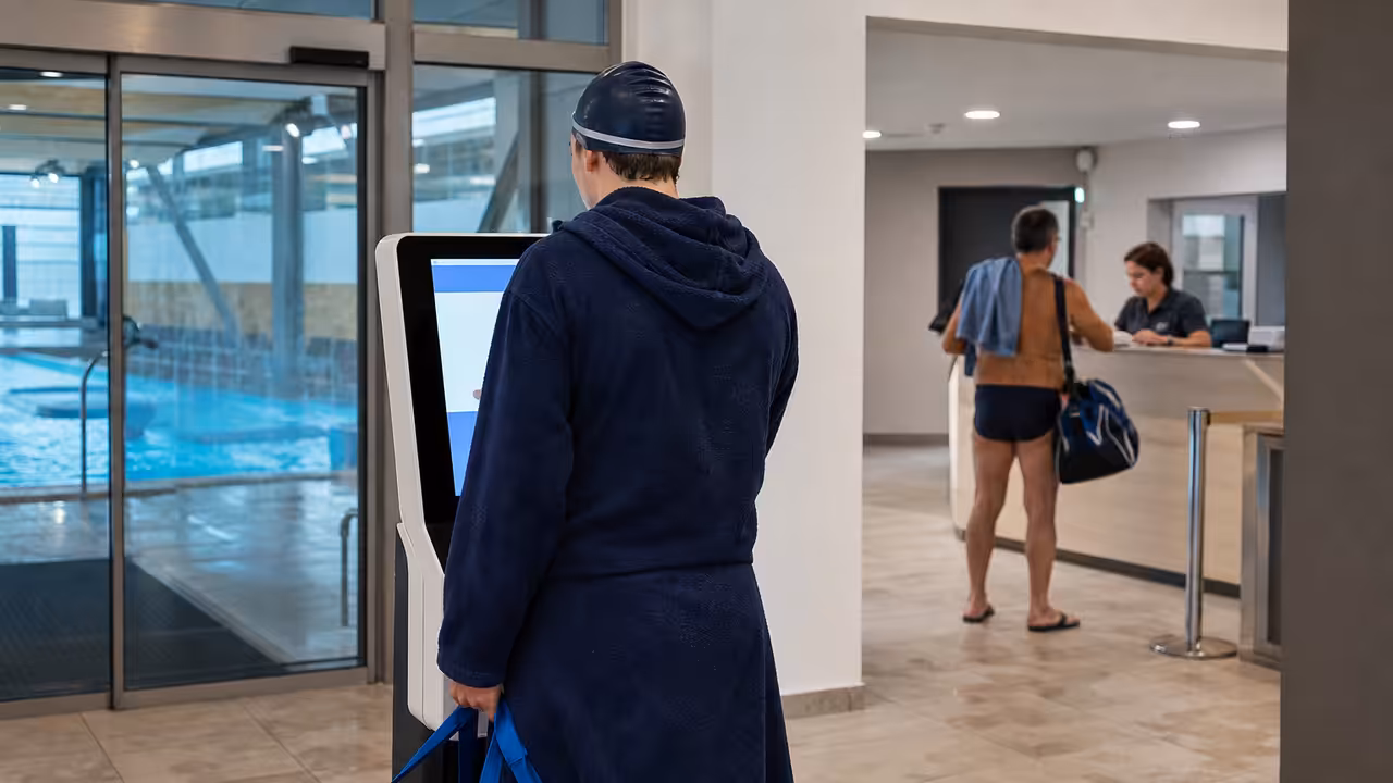 Usagers devant les bornes d’accueil d’une piscine municipale, préparant leur entrée avant une séance de nage