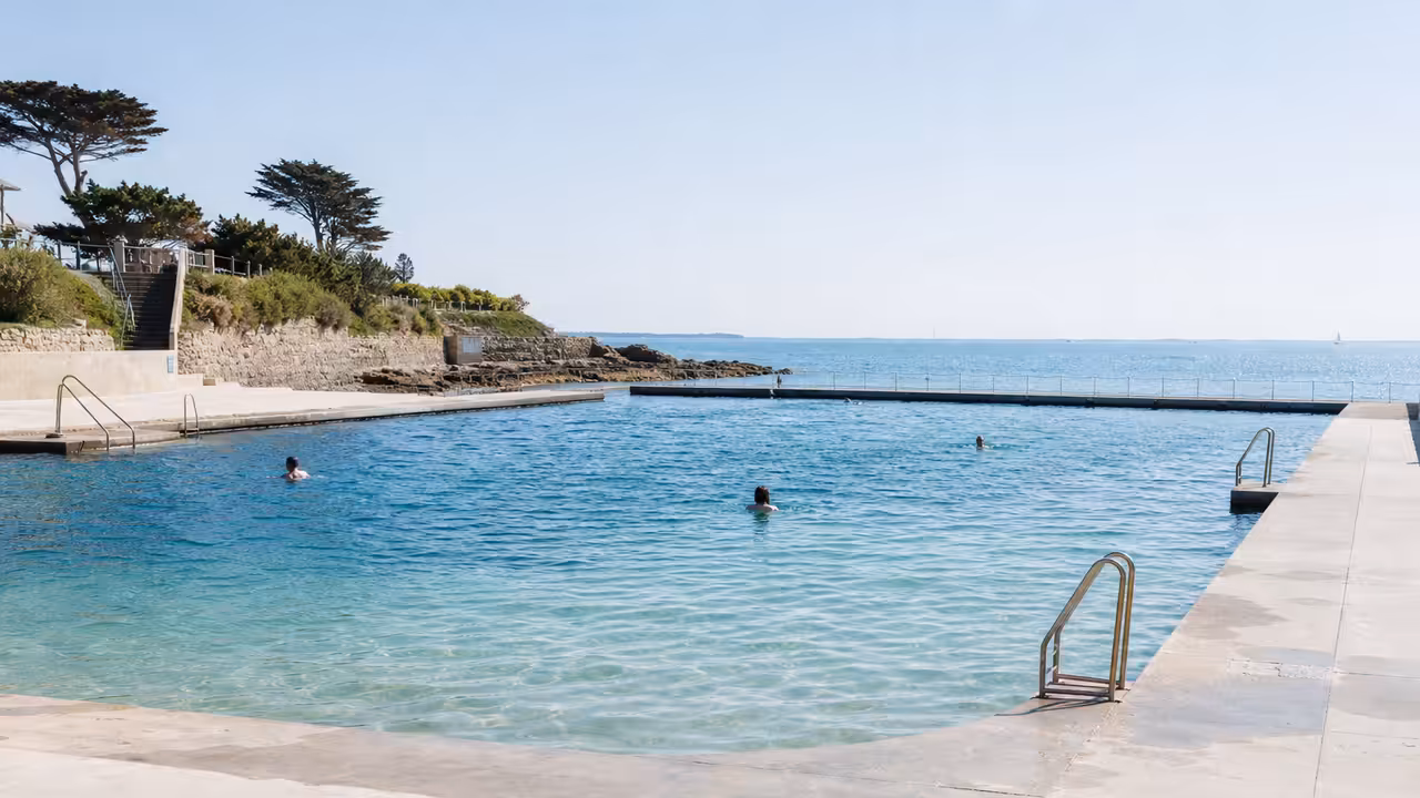 Bassin extérieur alimenté en eau de mer, plages minérales, accès sécurisés et végétation de bord de mer