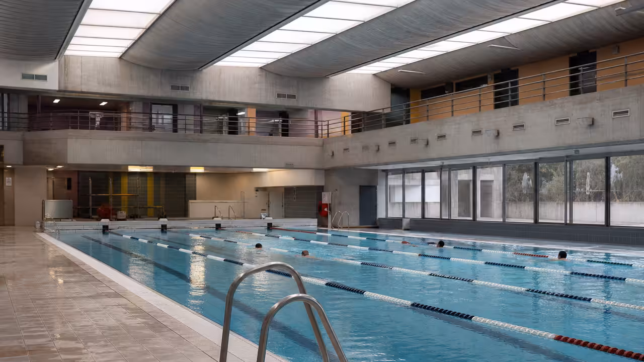 Bassin couvert d’une piscine municipale avec lignes d’eau dégagées et vestiaires visibles au fond
