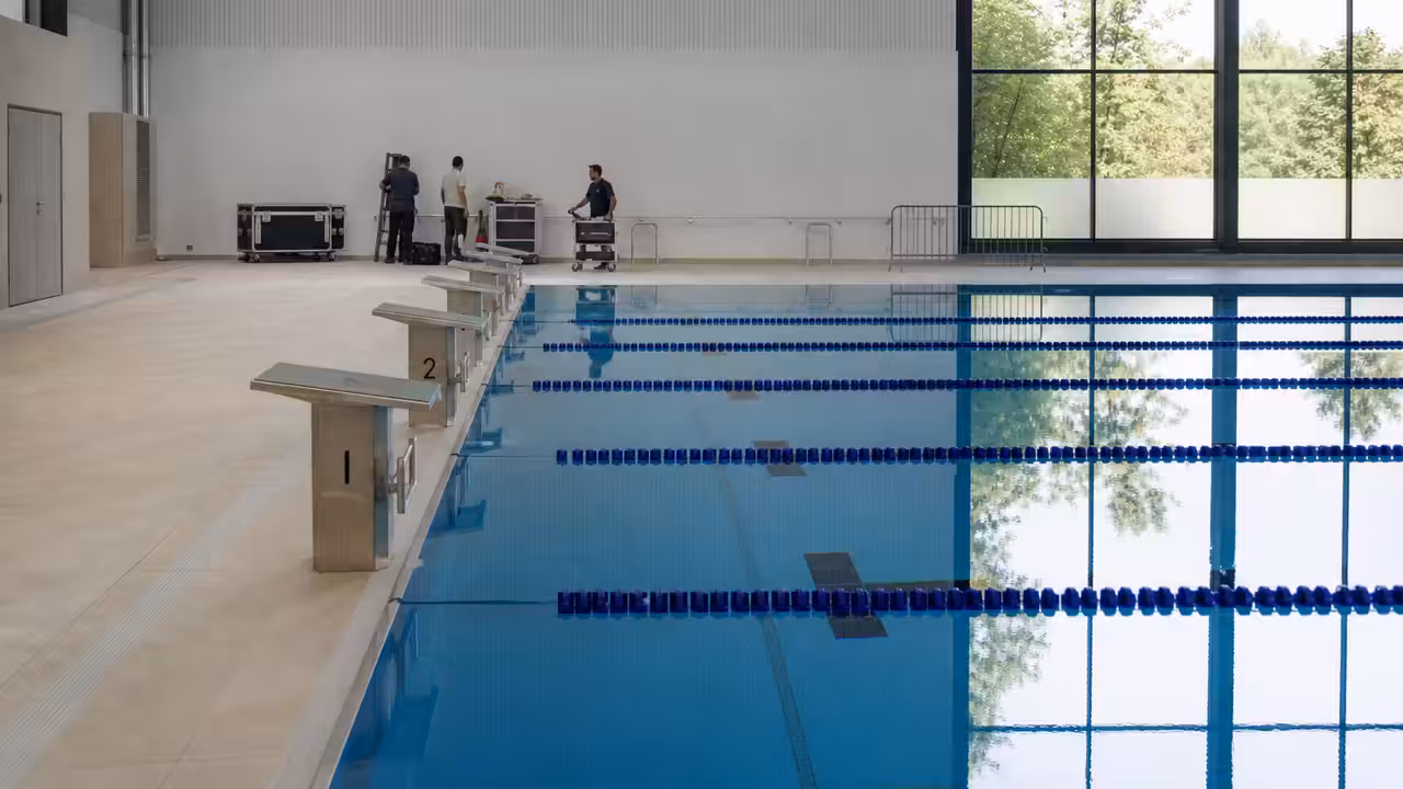Bassin municipal rénové et vide, avec lignes d’eau, plages claires et équipements techniques en préparation