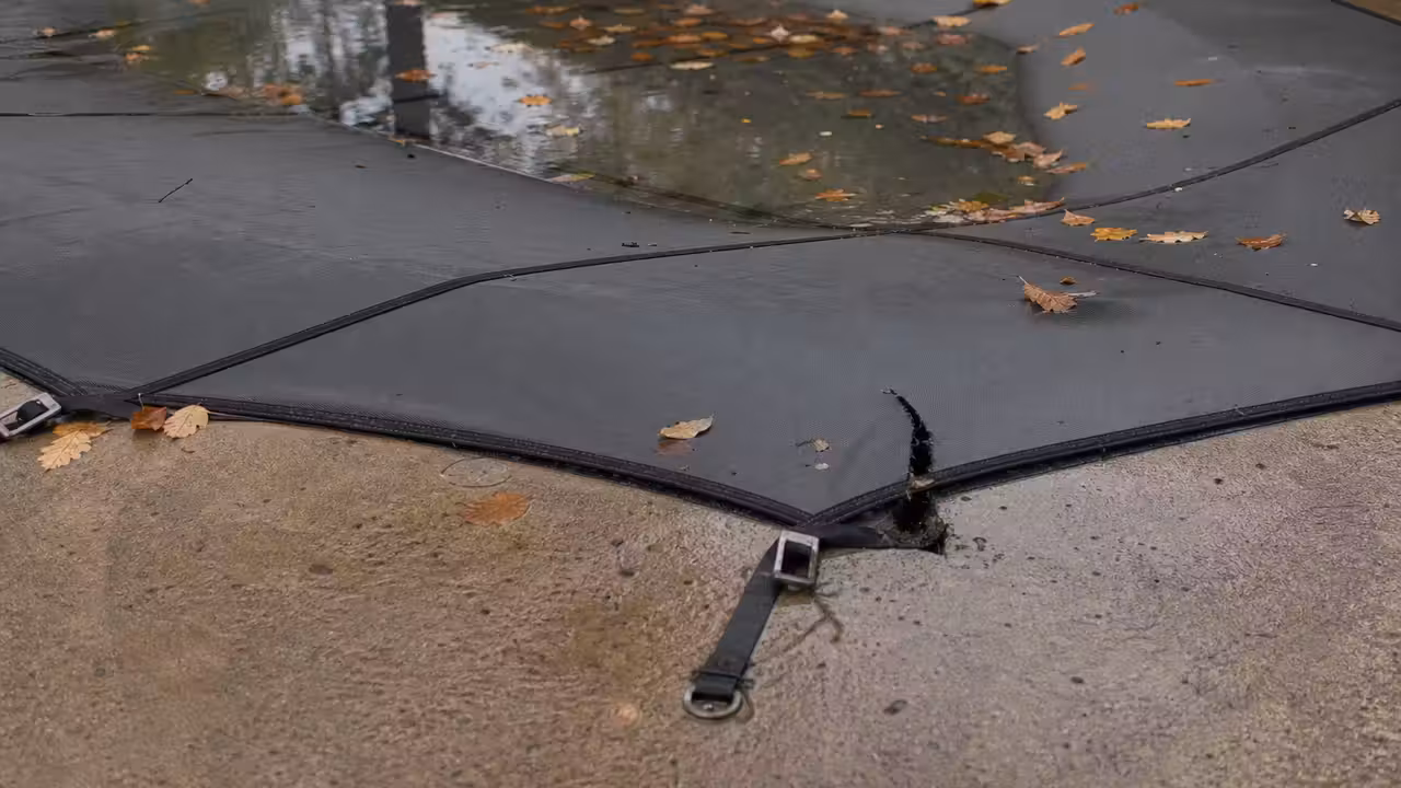 Bâche d'hivernage de piscine tendue avec une poche d'eau de pluie visible et une déchirure sur un bord