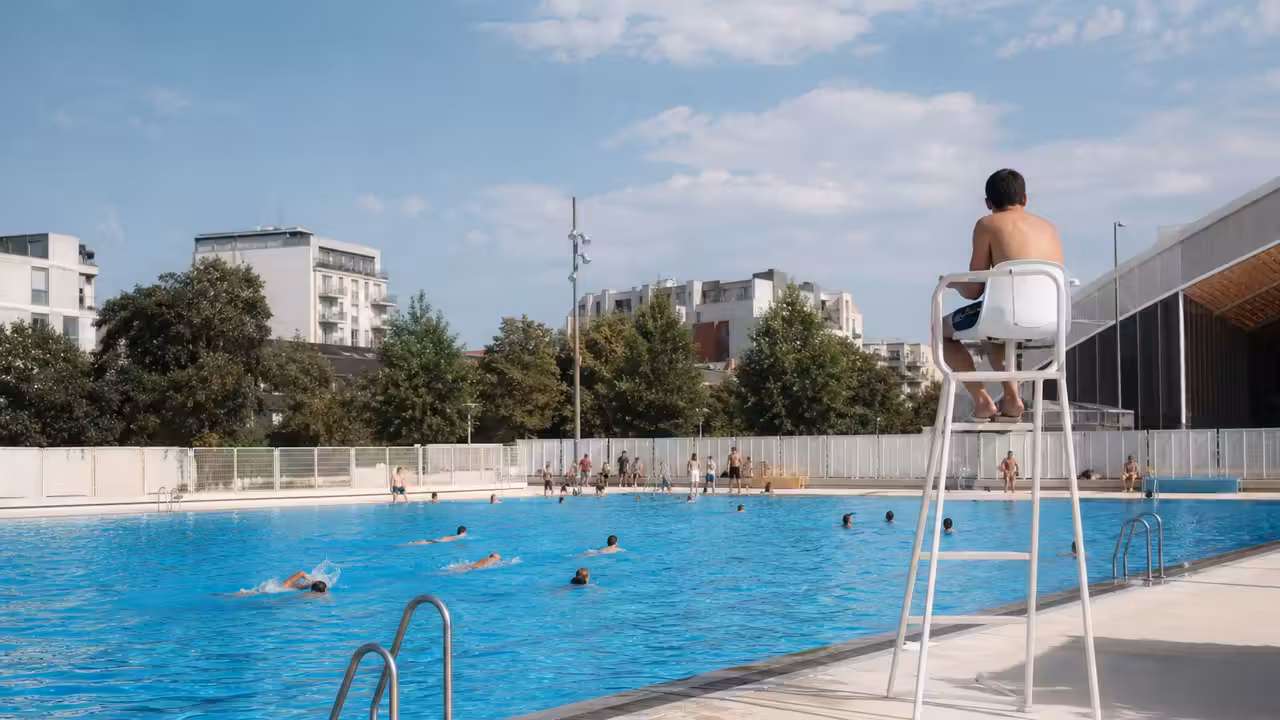 Bassin extérieur temporaire dans un centre sportif parisien, avec nageurs et zone de repos au soleil