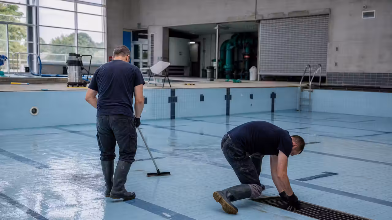 Bassin intérieur vidé lors d’une maintenance annuelle, avec des techniciens nettoyant les parois et le fond