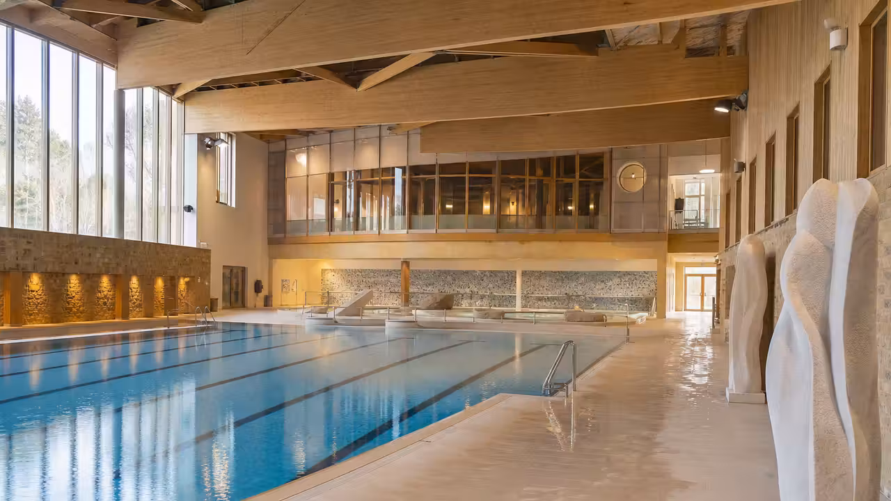 Bassin intérieur lumineux d’une piscine publique avec sculptures minérales et larges baies vitrées