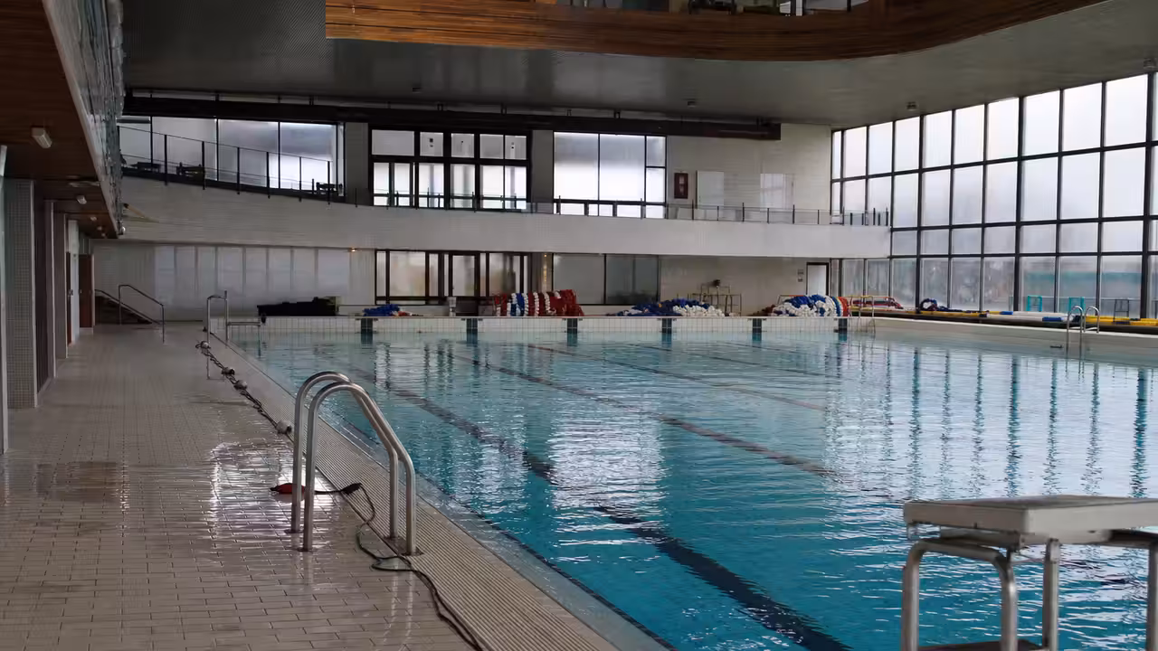Bassin municipal couvert vide, lignes d’eau retirées et lumière naturelle sur les carrelages humides