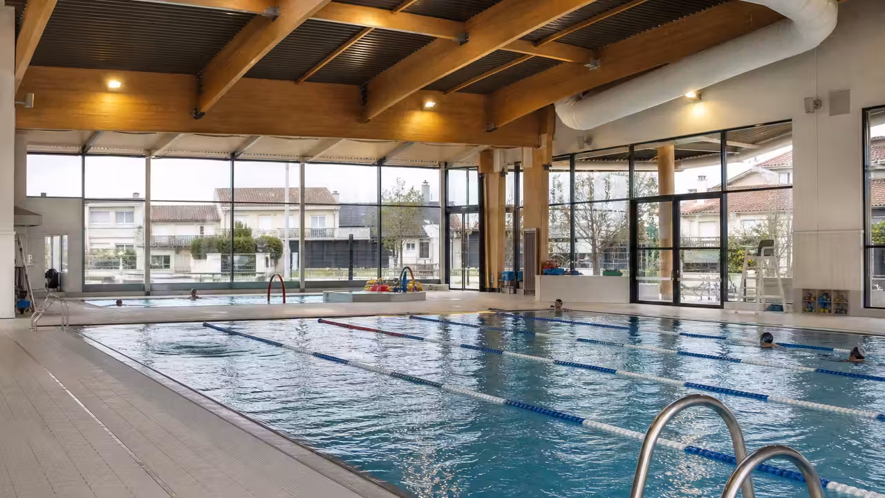 Vue intérieure d’un centre aquatique municipal moderne avec bassin de nage, baies vitrées et plages accessibles