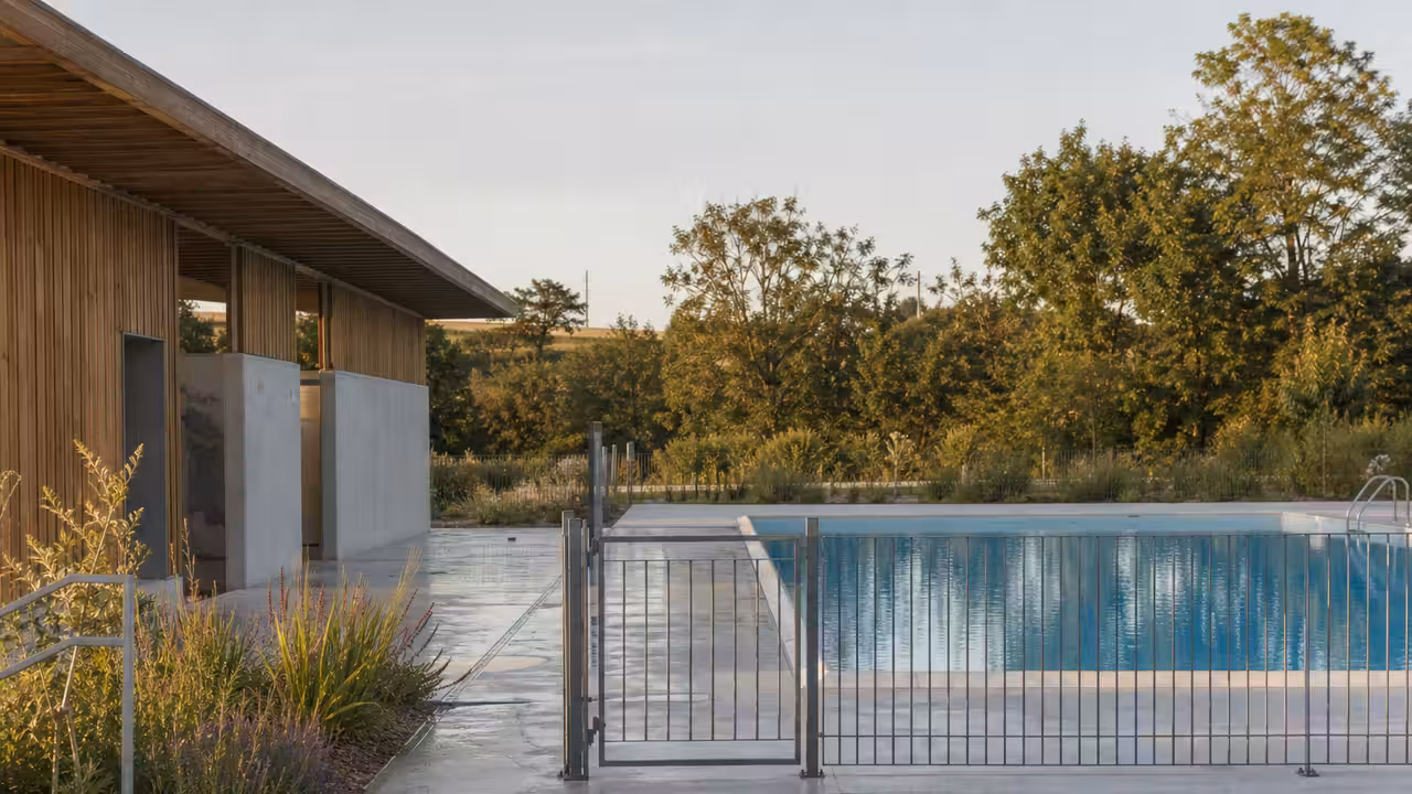 Bassin extérieur d’une piscine municipale rénovée, bordé de plages minérales et d’arbres
