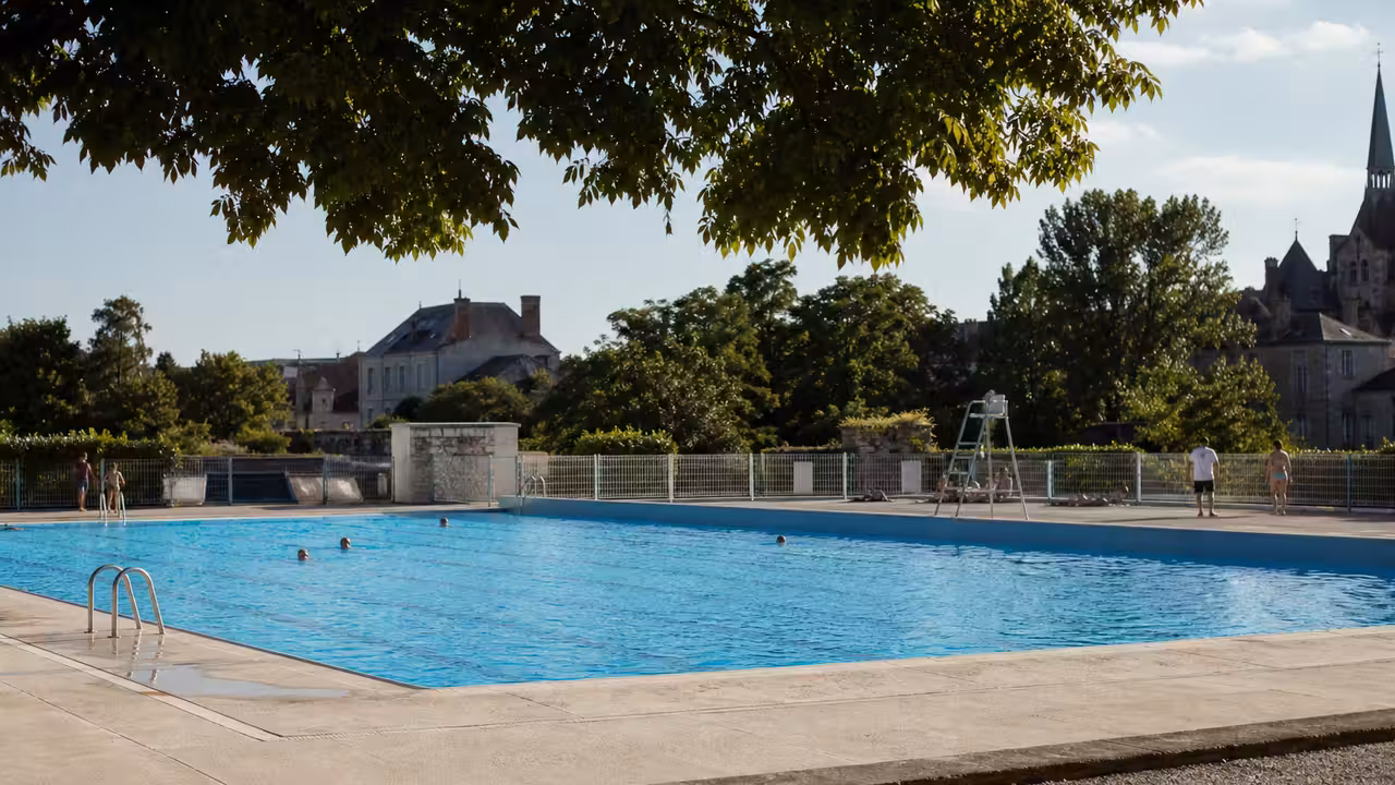Bassin extérieur d’une piscine municipale avec lignes d’eau, pelouse et baigneurs à distance en été