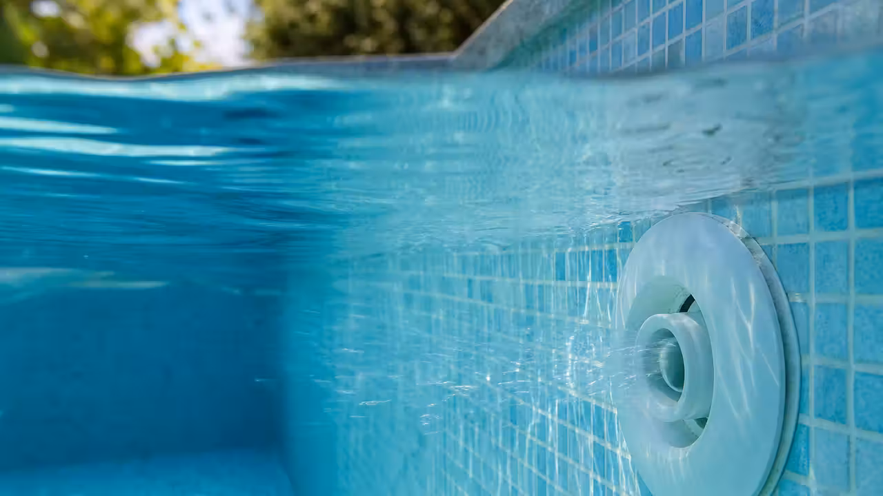 Buse de refoulement de piscine visible sous la surface de l'eau, paroi et carrelage autour de la pièce scellée