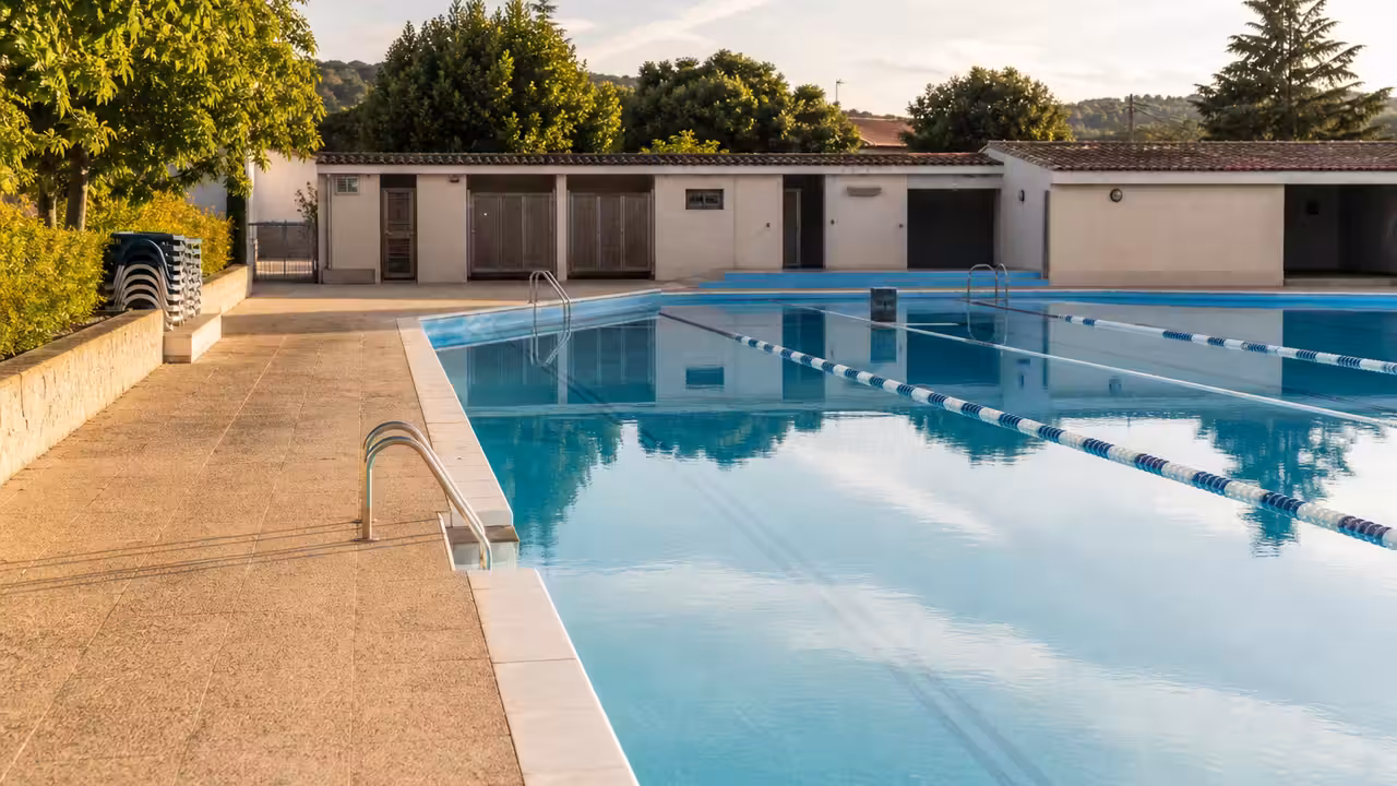 Bassin extérieur municipal calme en fin de journée, avec lignes d’eau et plages bordées d’arbres