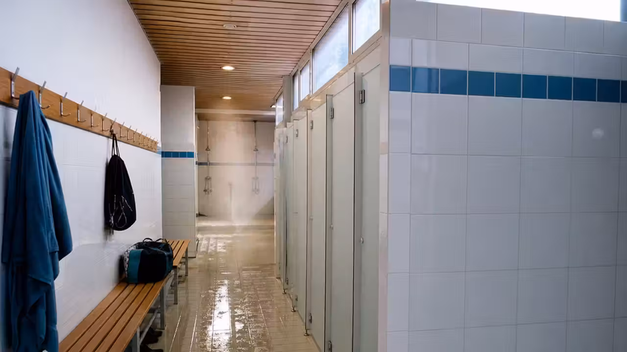 Vestiaires chauffés d’une piscine municipale avec rangée de douches et bancs, sans usager identifiable