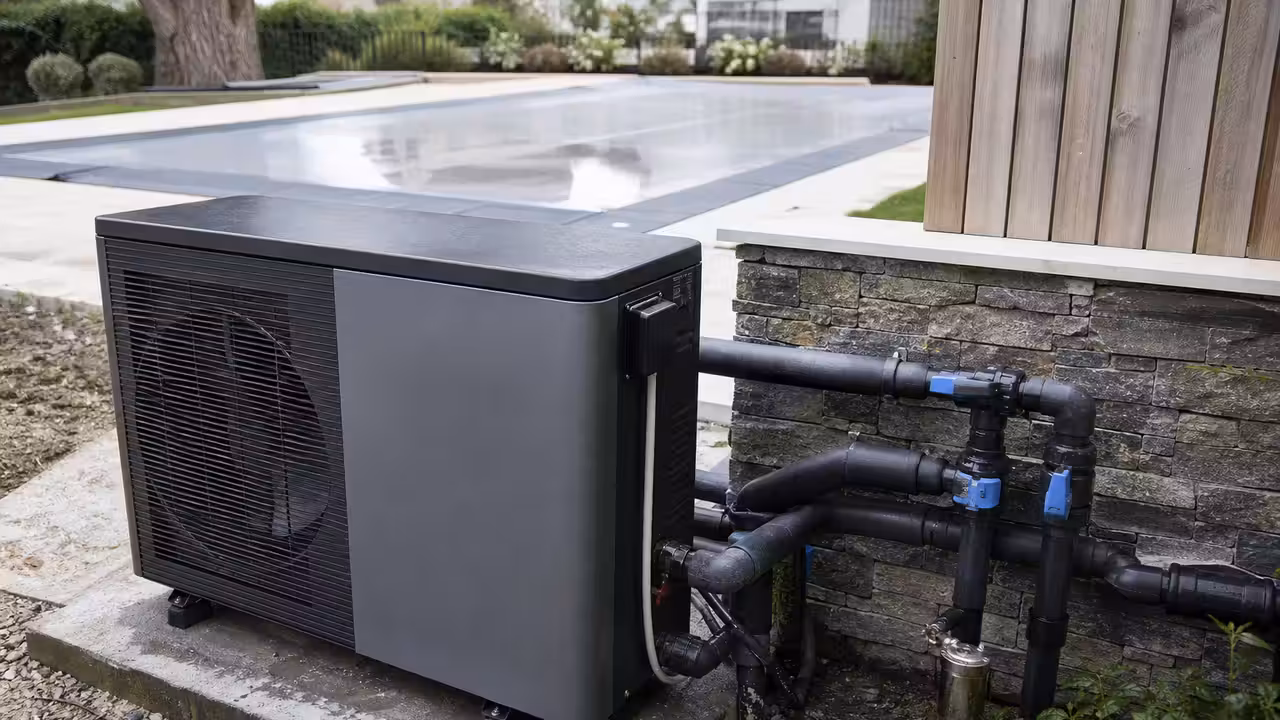Pompe à chaleur installée près d’un local technique, devant une piscine extérieure couverte