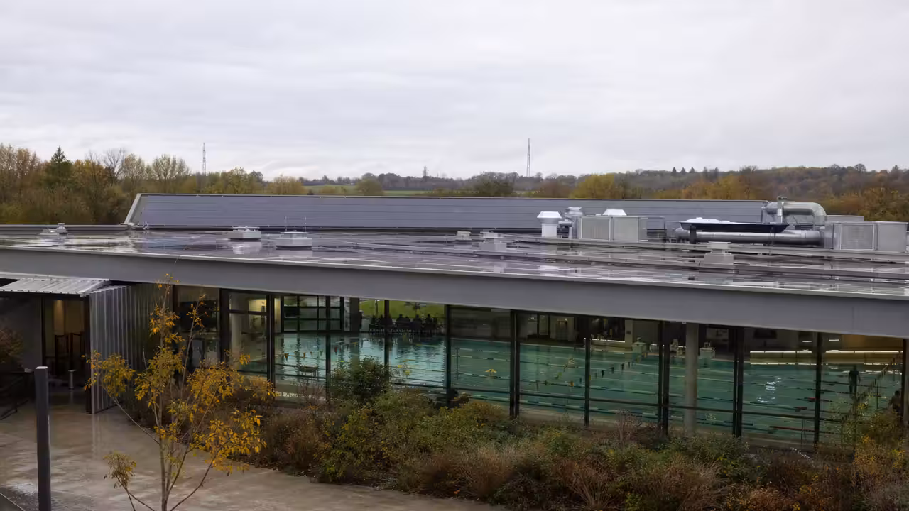 Hall de bassin d’une piscine municipale avec toiture vitrée et équipements techniques de ventilation discrets