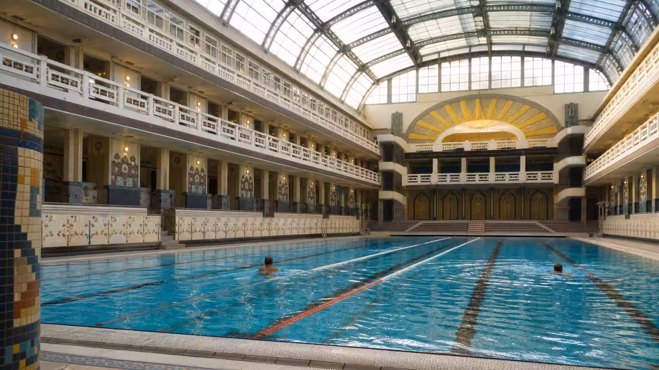 Bassin couvert Art déco avec verrière, mosaïques colorées et lignes de nage dans une piscine parisienne