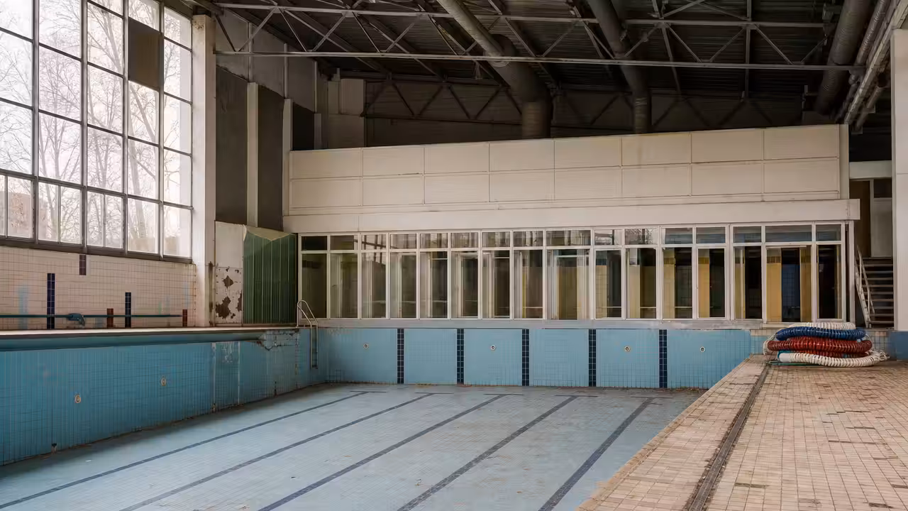 Bassin extérieur municipal vide, avec lignes d’eau retirées et équipements techniques vieillissants en arrière-plan