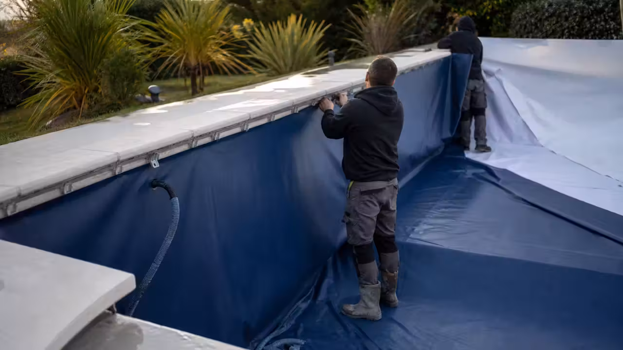 Pose d’un liner bleu dans une piscine rectangulaire vide, avec feutre de protection et margelles en pierre