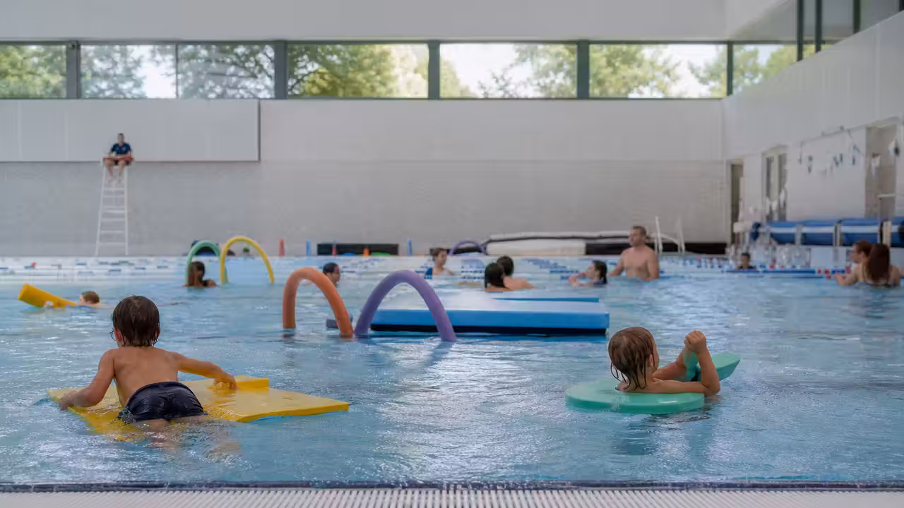 Enfants accompagnés par des adultes dans un bassin ludique d’une piscine publique couverte