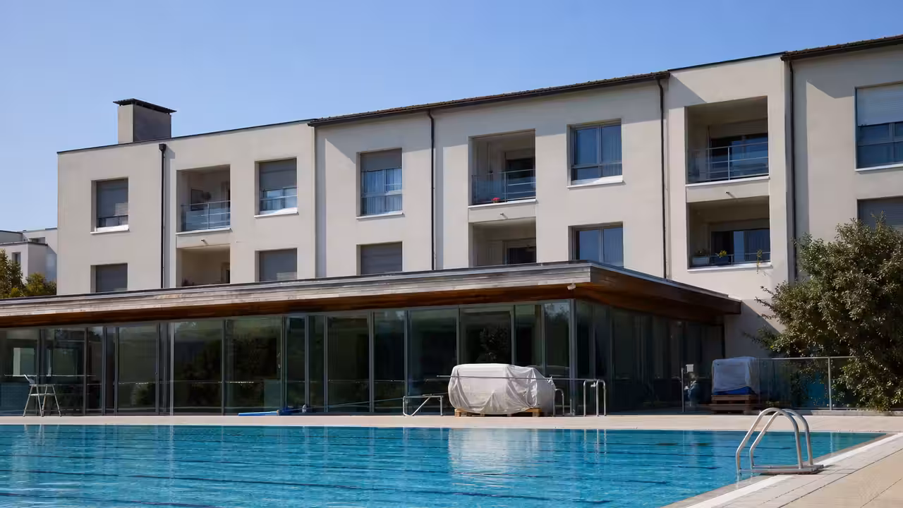 Façade d’une piscine municipale avec fenêtres d’un appartement à l’étage et bassin extérieur au premier plan