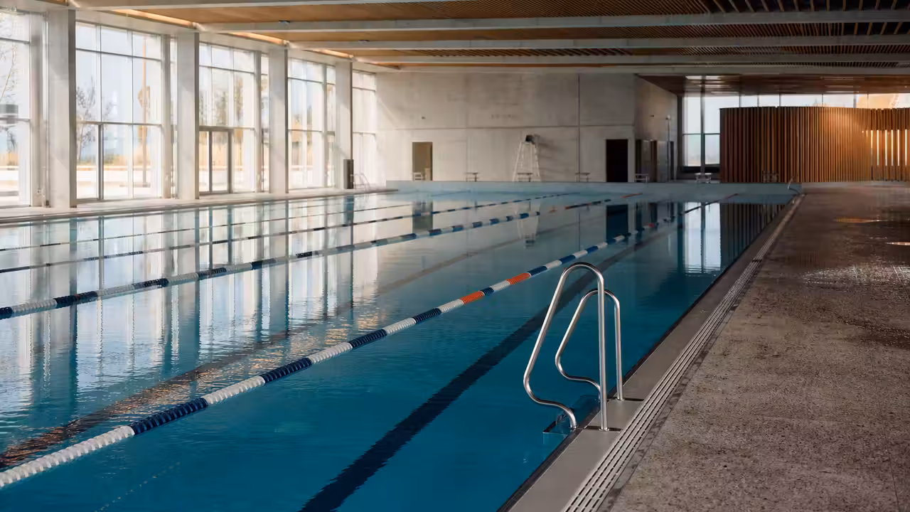 Bassin sportif de 50 mètres dans un centre aquatique public lumineux, avec lignes d’eau et gradins