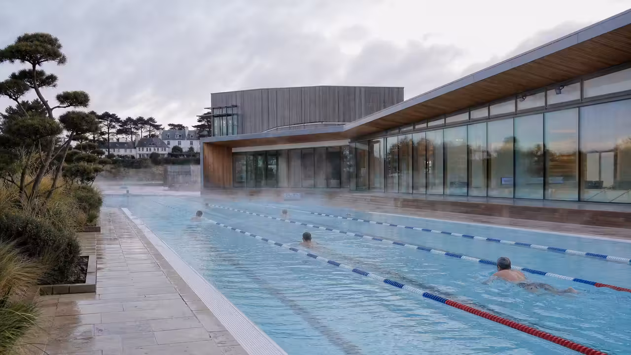 Bassin extérieur d’un centre aquatique municipal avec lignes de nage et bâtiment rénové à l’arrière-plan