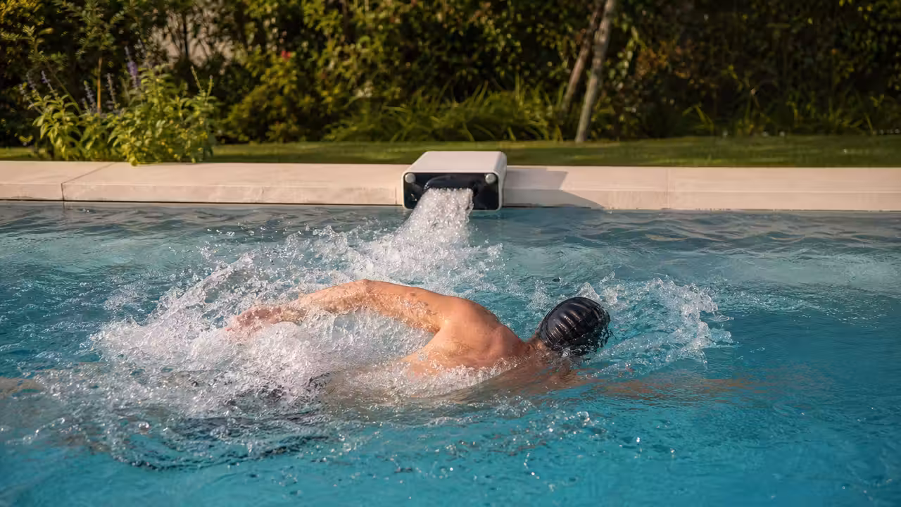 Nageur adulte s’exerçant face à un jet de nage installé sur la margelle d’une piscine privée