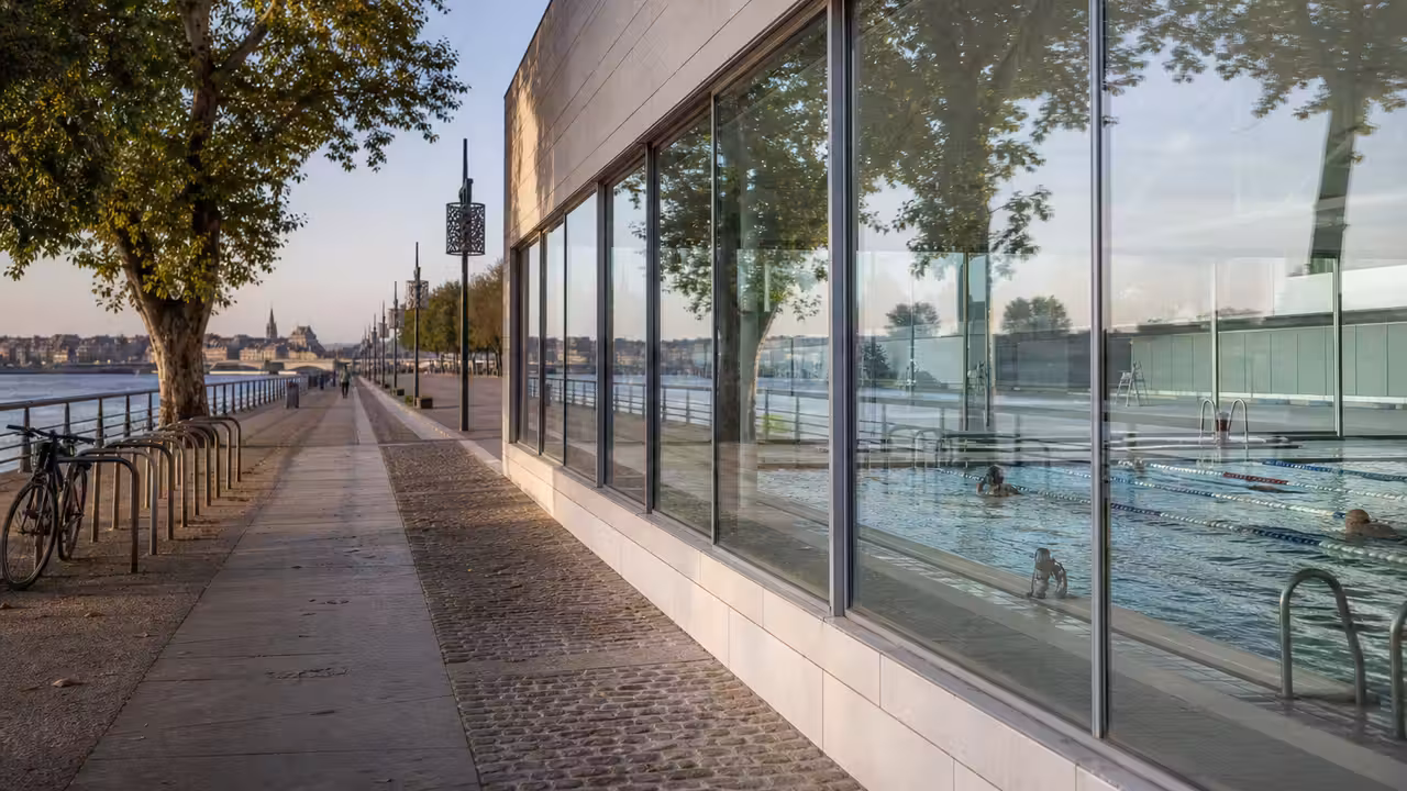 Vue d’un centre aquatique contemporain au bord des quais bordelais avec bassin de nage et espaces vitrés.