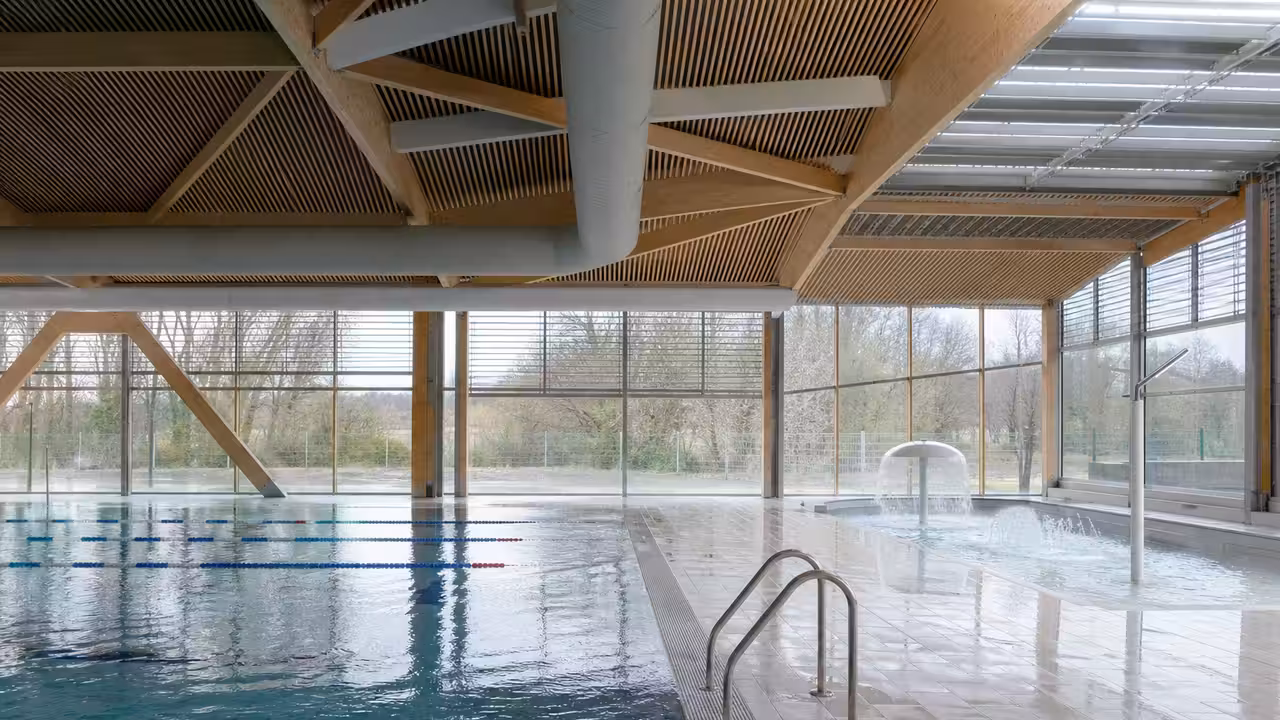 Bassin sportif couvert de 25 mètres dans un centre aquatique contemporain, avec baies vitrées et lignes d’eau