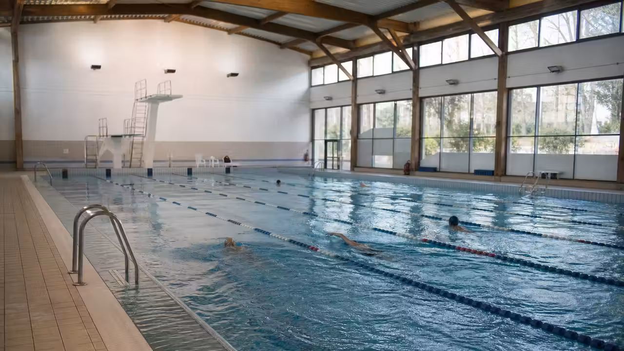 Bassin sportif couvert de 25 mètres avec six couloirs, gradins sobres et lumière du jour à Périgueux