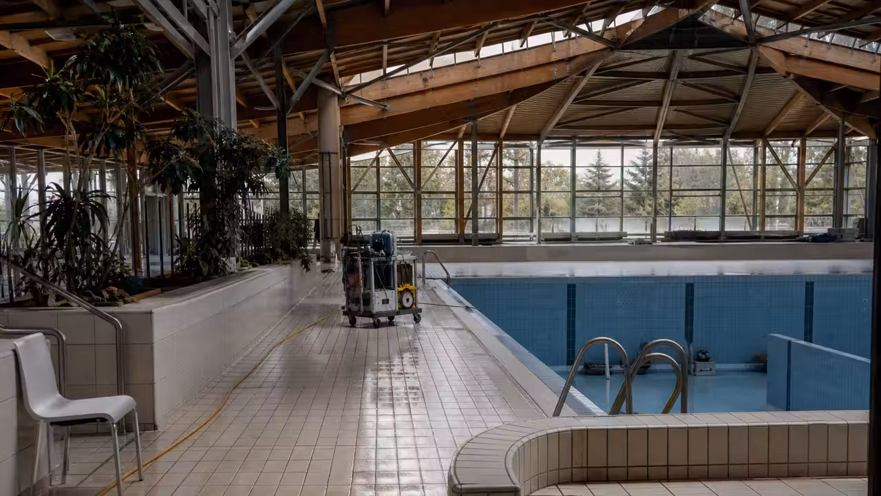 Entrée vitrée d’une piscine municipale fermée pendant une maintenance, bassin visible à l’arrière-plan