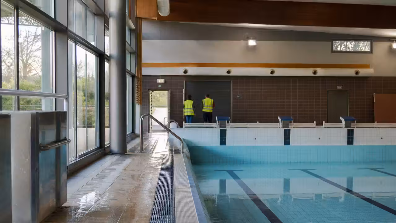 Halle de piscine municipale vide, avec bassin couvert et personnel contrôlant les installations techniques