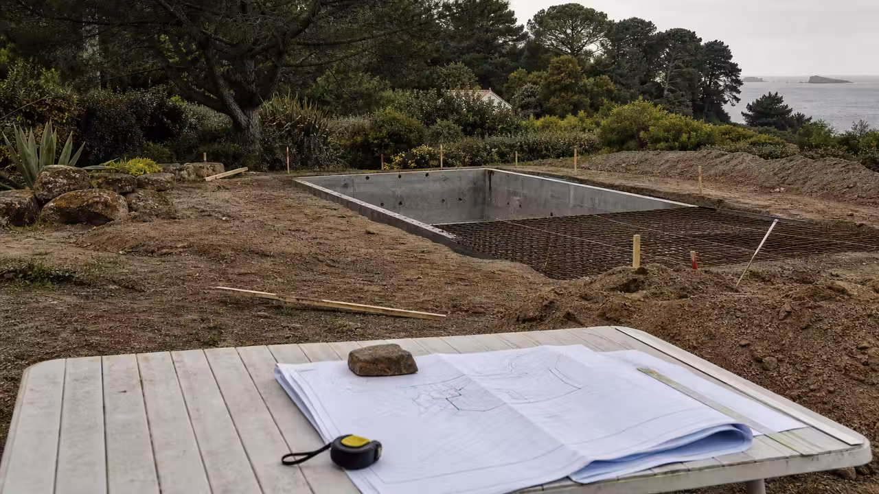 Piscine enterrée en chantier près d’un jardin boisé, avec plans d’urbanisme consultés sur une table