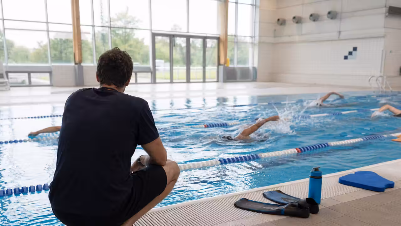 Entraîneur observant des nageurs adultes pendant une séance technique dans une piscine couverte