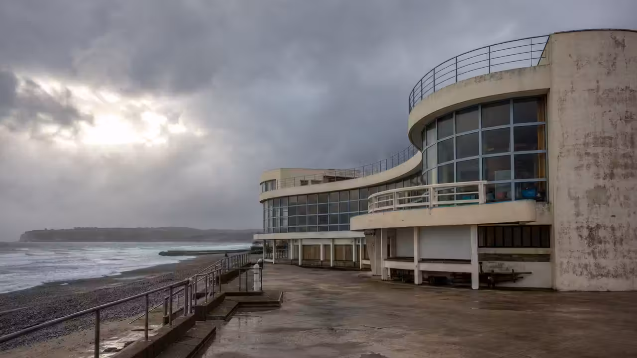 Ancien bassin de piscine publique en bord de mer, avec architecture balnéaire et ciel normand lumineux