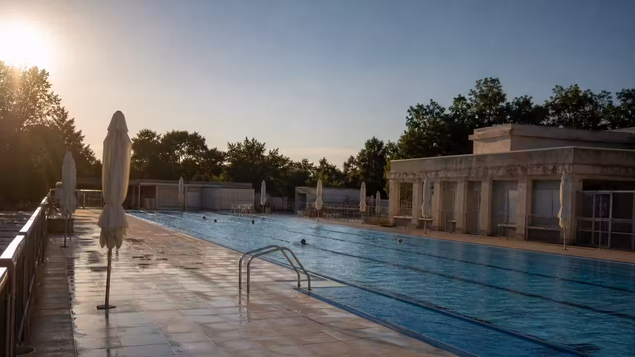 Bassin extérieur d'une piscine municipale en été, lignes d'eau et plage presque vide en fin d'après-midi