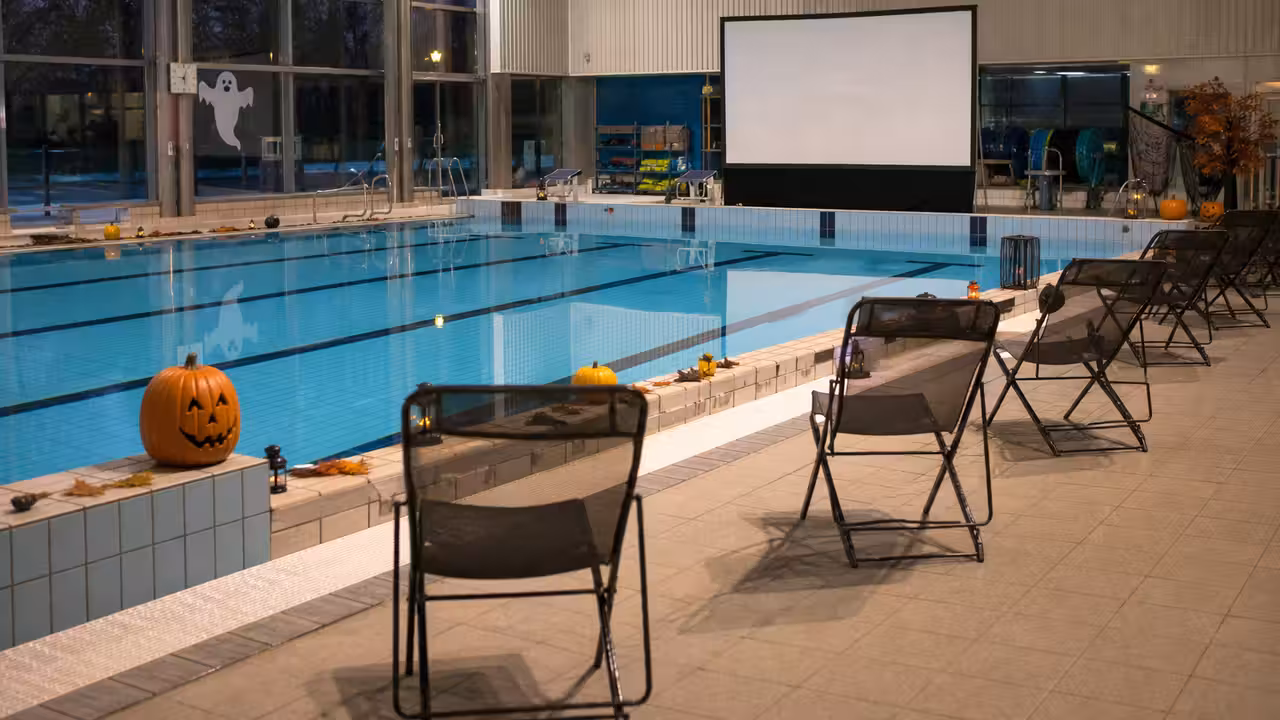 Écran de cinéma installé au bord d’un bassin municipal éclairé en soirée pour une animation aquatique