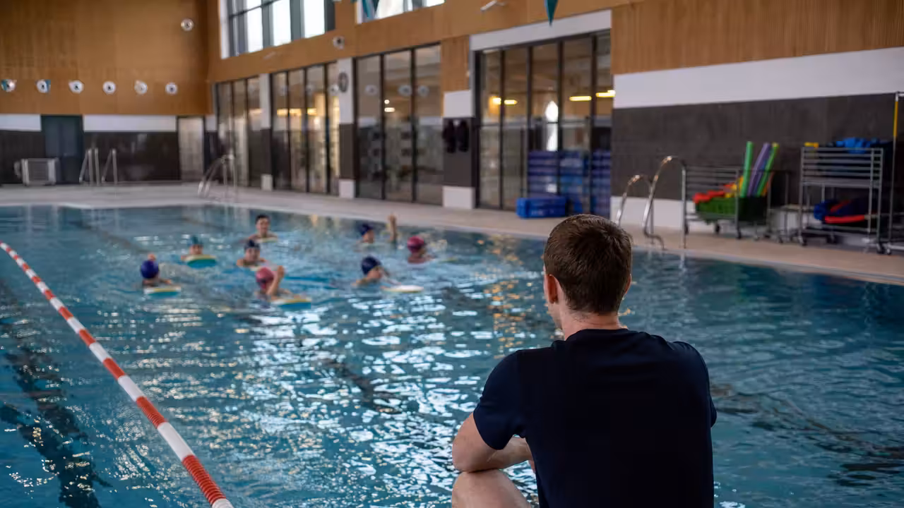 Bassin intérieur municipal avec lignes d’eau et groupe d’enfants encadrés lors d’une séance de natation