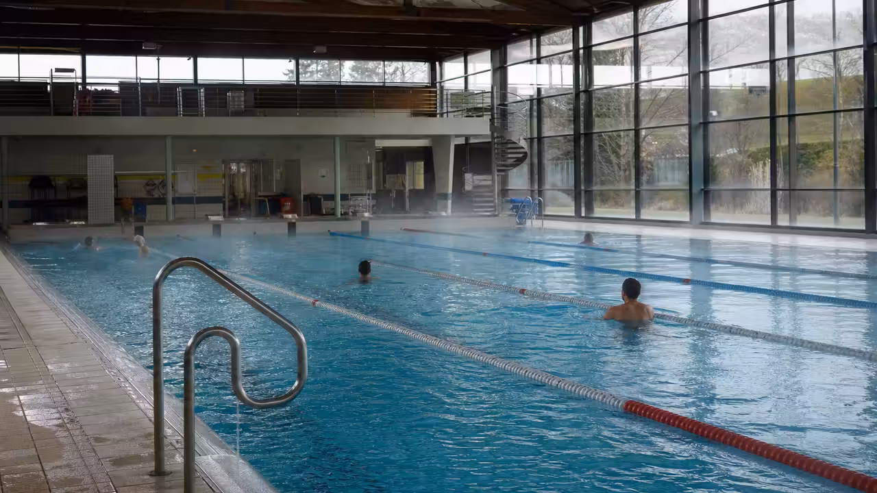 Bassin intérieur d’une piscine publique avec lignes d’eau, éclairage naturel et nageurs à distance
