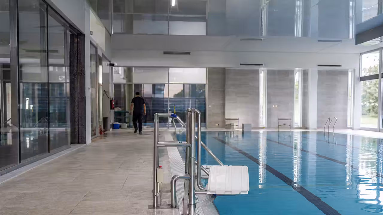 Bassin intérieur municipal avec couloirs de nage, vestiaires rénovés et larges baies vitrées lumineuses